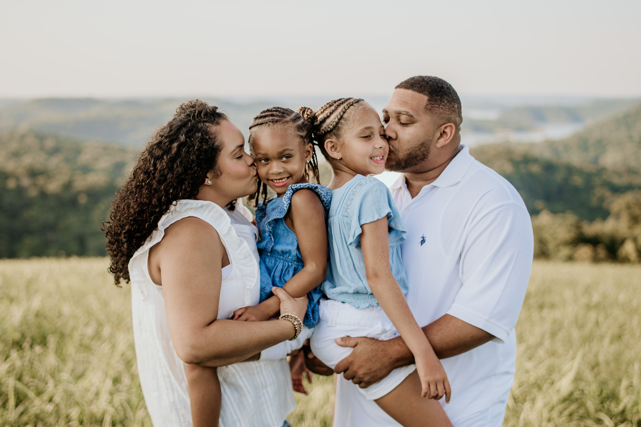 A family portrait of a mother and father holding their smiling daughters between them.