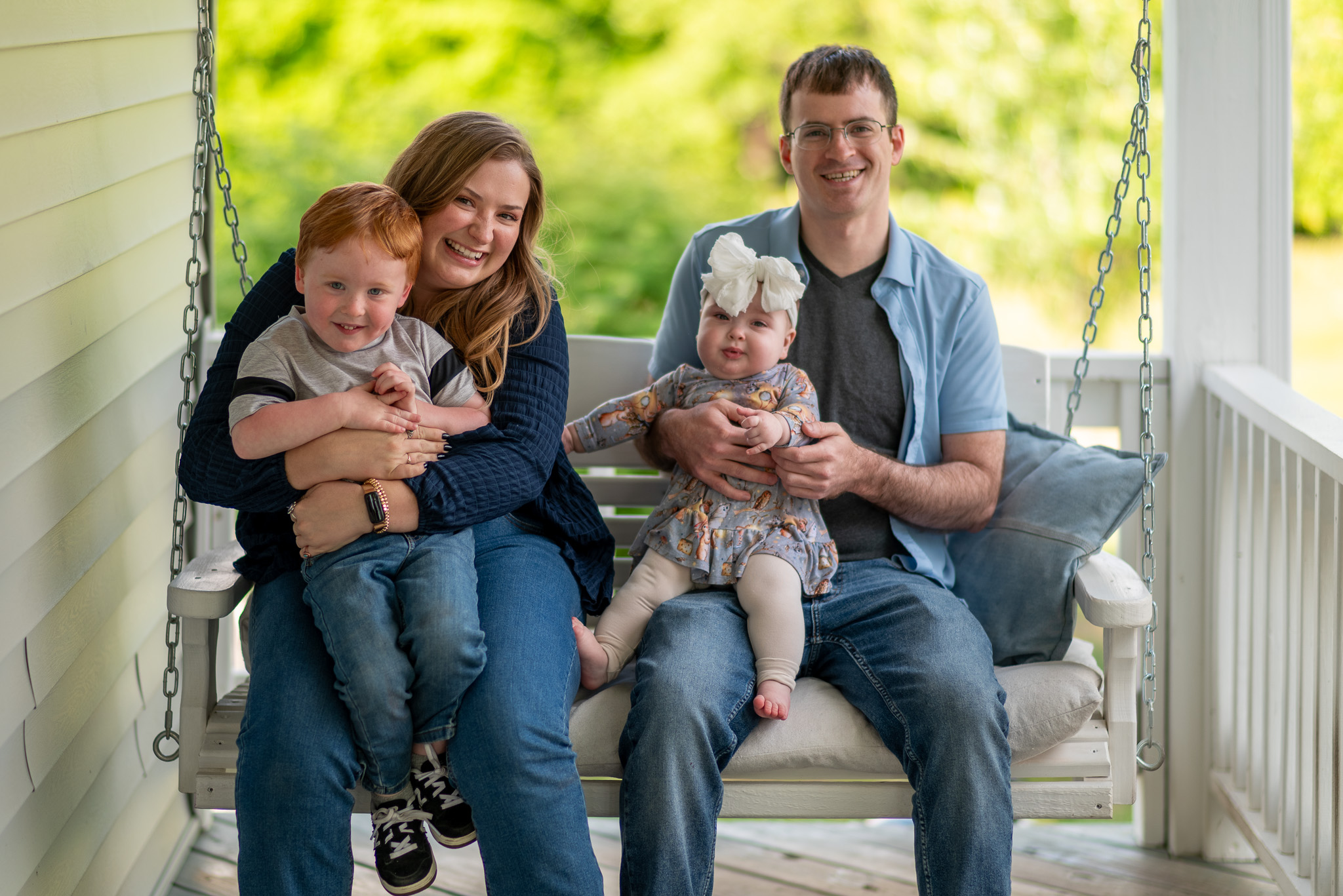 A family portrait of a young woman and a young man holding their nephew and niece on a porch swing.